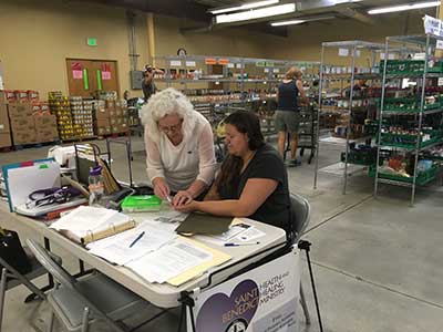 Woman assisting another woman with a blood sugar test as a part of basic health care free clinics put on by St. Benedict Health and Healing Ministry.